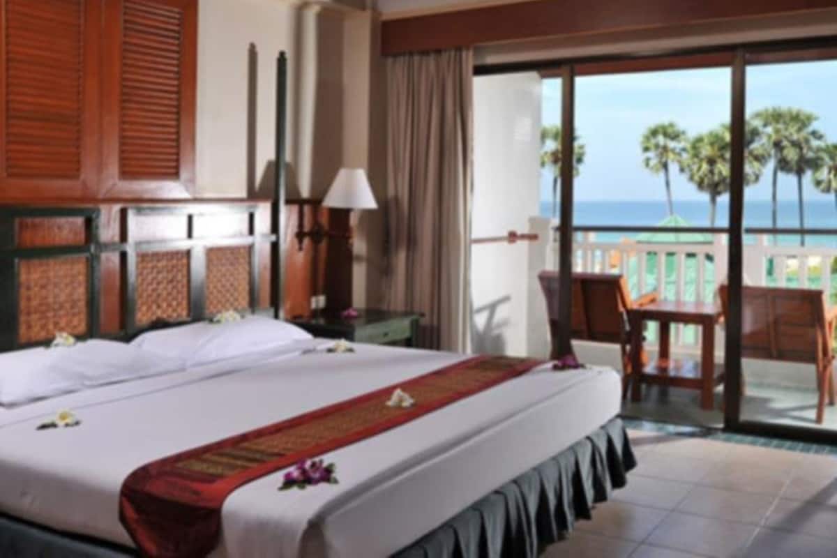 A hotel room with a large bed, a balcony with a table and chairs, and a view of the ocean.