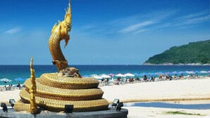 A golden dragon statue on a beach with umbrellas and people in the background. - Karon Princess Hotel (Karon)