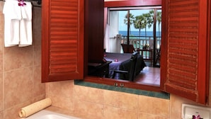 A bathroom with a bathtub filled with rose petals, a mirror reflecting a balcony with a view of the ocean, and wooden shutters on the windows. - Karon Princess Hotel (Karon)
