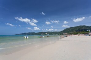 Une plage à l’eau claire, avec des bateaux et un paysage vallonné en arrière-plan.