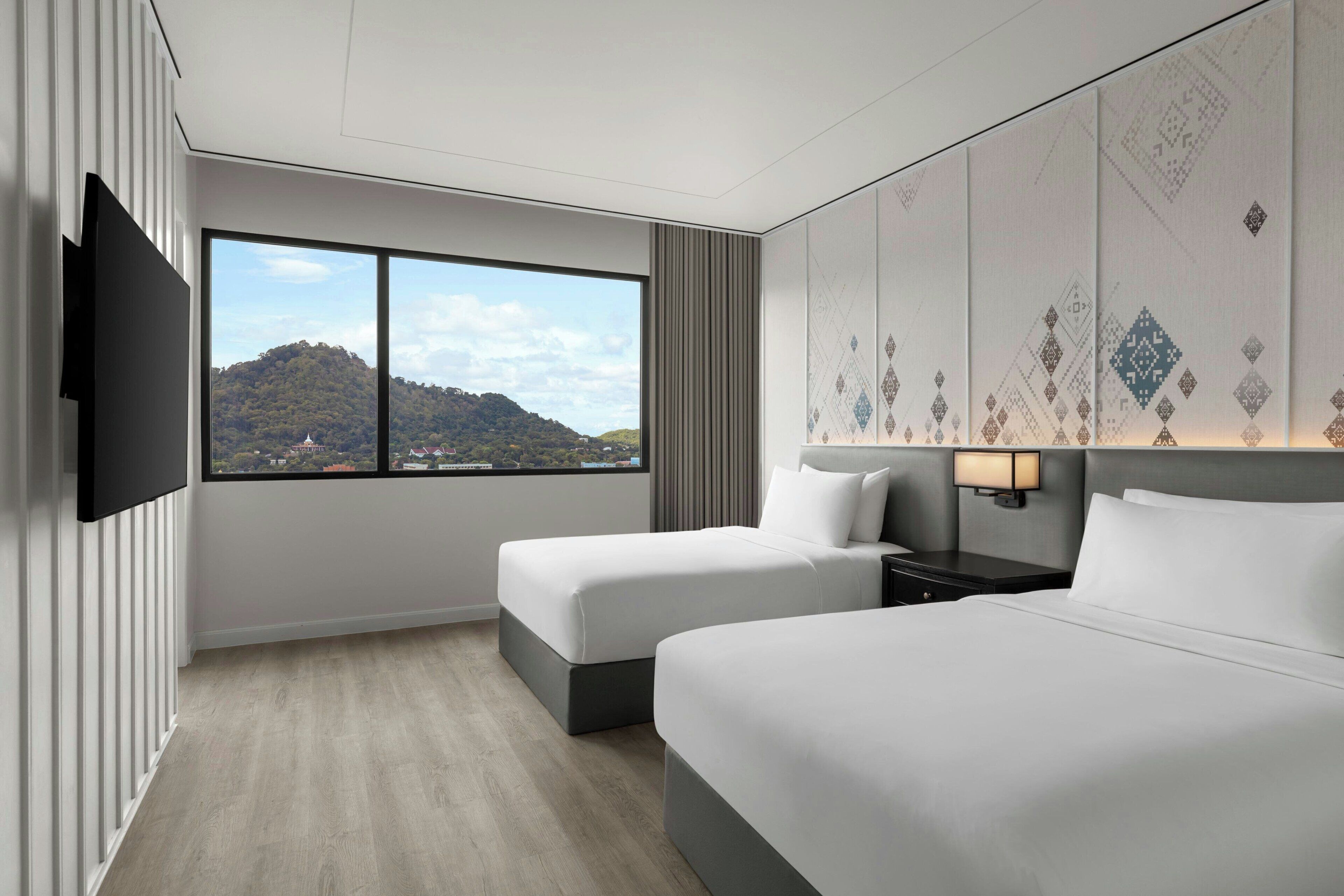 Habitación de hotel con dos camas, un ventanal con vistas a la montaña, un televisor de pantalla plana y una lámpara de pared.