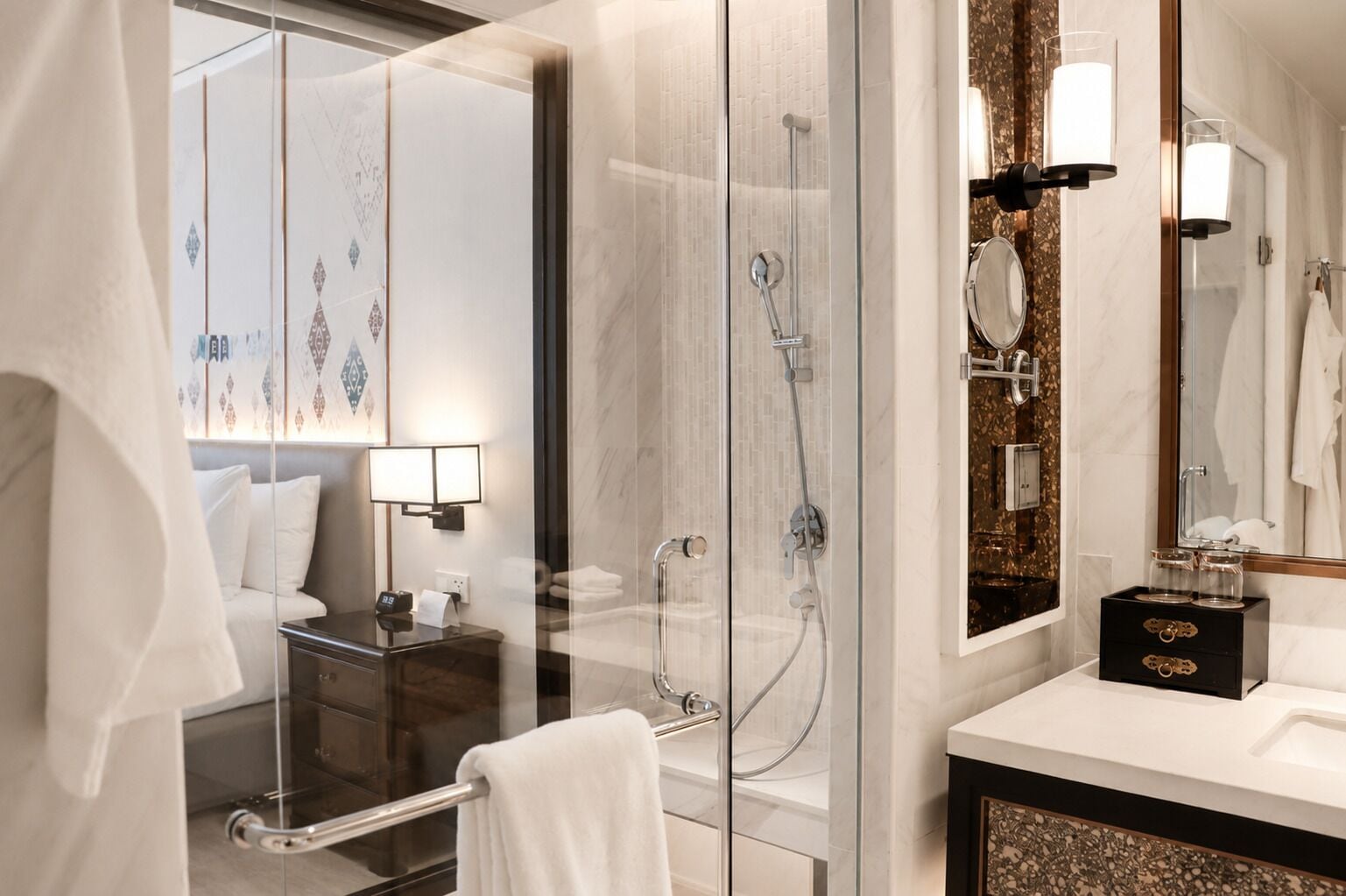 A modern bathroom with a glass-enclosed shower, a vanity with a mirror, and a bed with a nightstand.