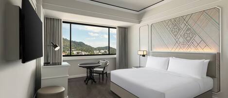 A modern hotel room with a large bed, a desk, a chair, a TV, and a window with a city view.