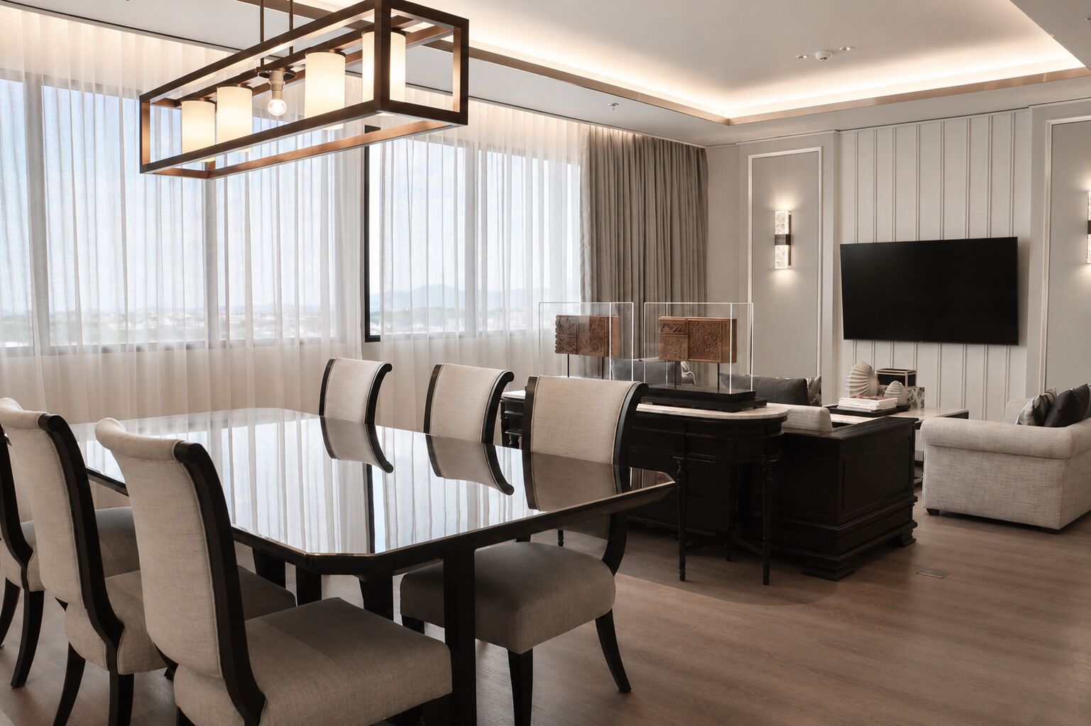 Una habitación de hotel moderna con una mesa de comedor, sillas, un sofá, un televisor y un ventanal con cortinas.