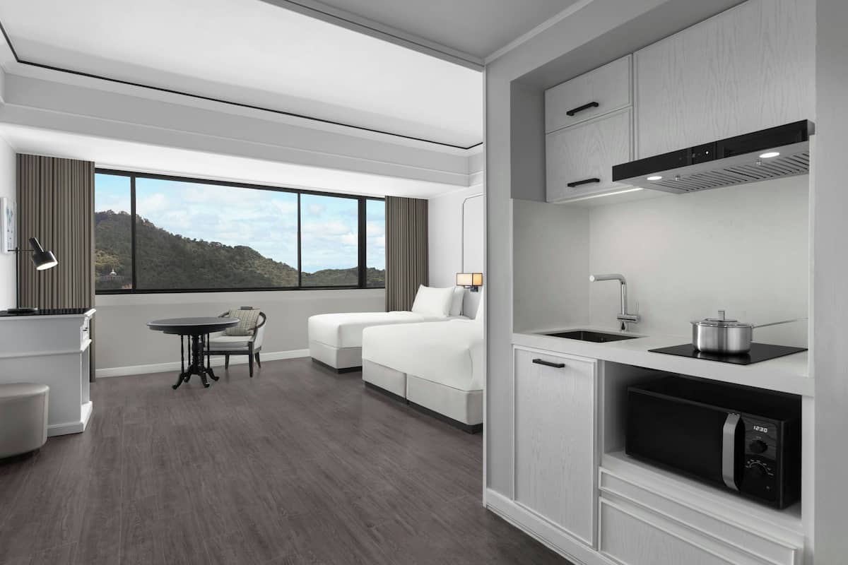 Une chambre d’hôtel moderne dotée d’une grande fenêtre, d’une kitchenette, d’un canapé et d’un coin repas.