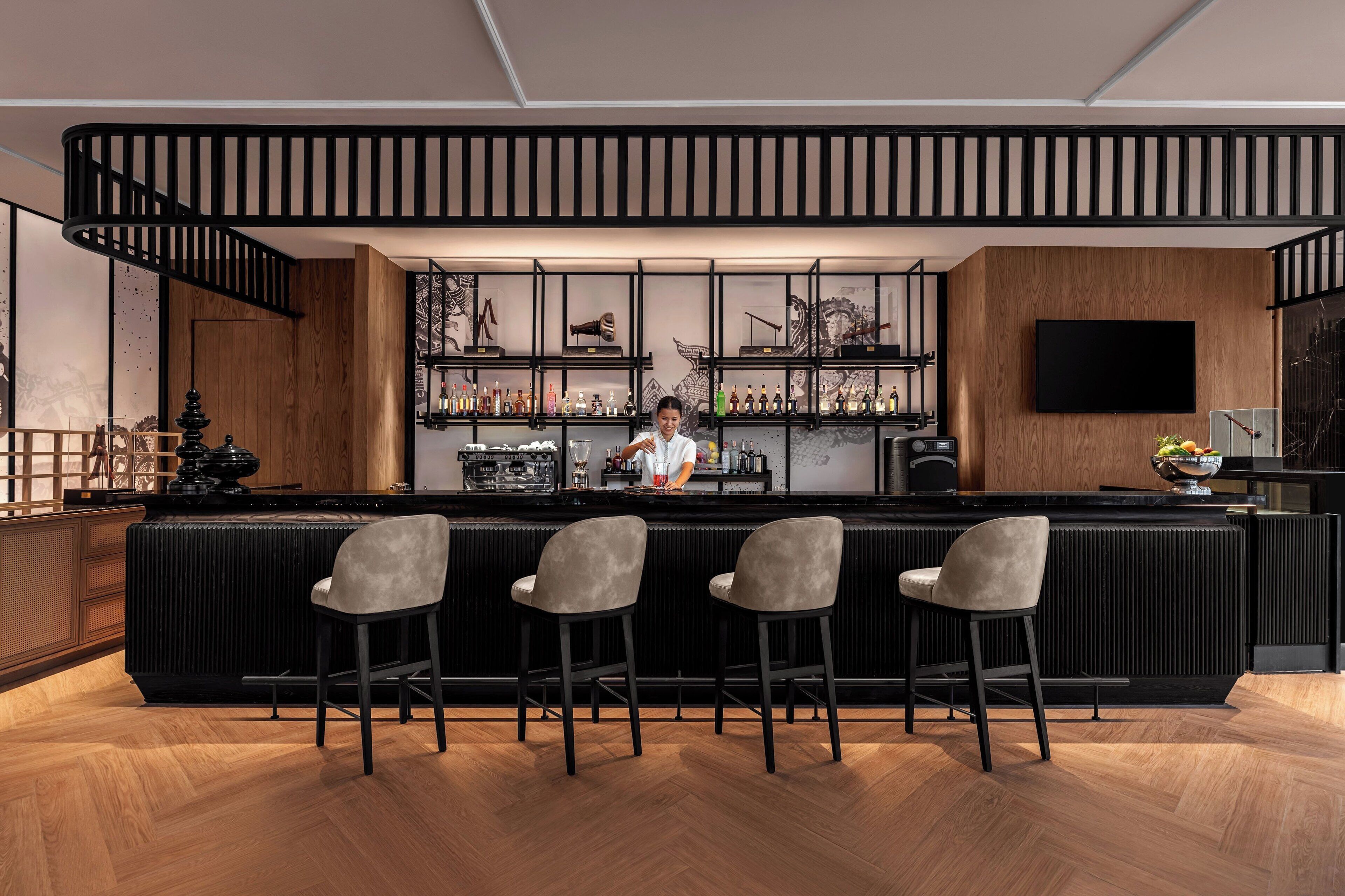 A modern bar area with a wooden counter, bar stools, and a bartender.