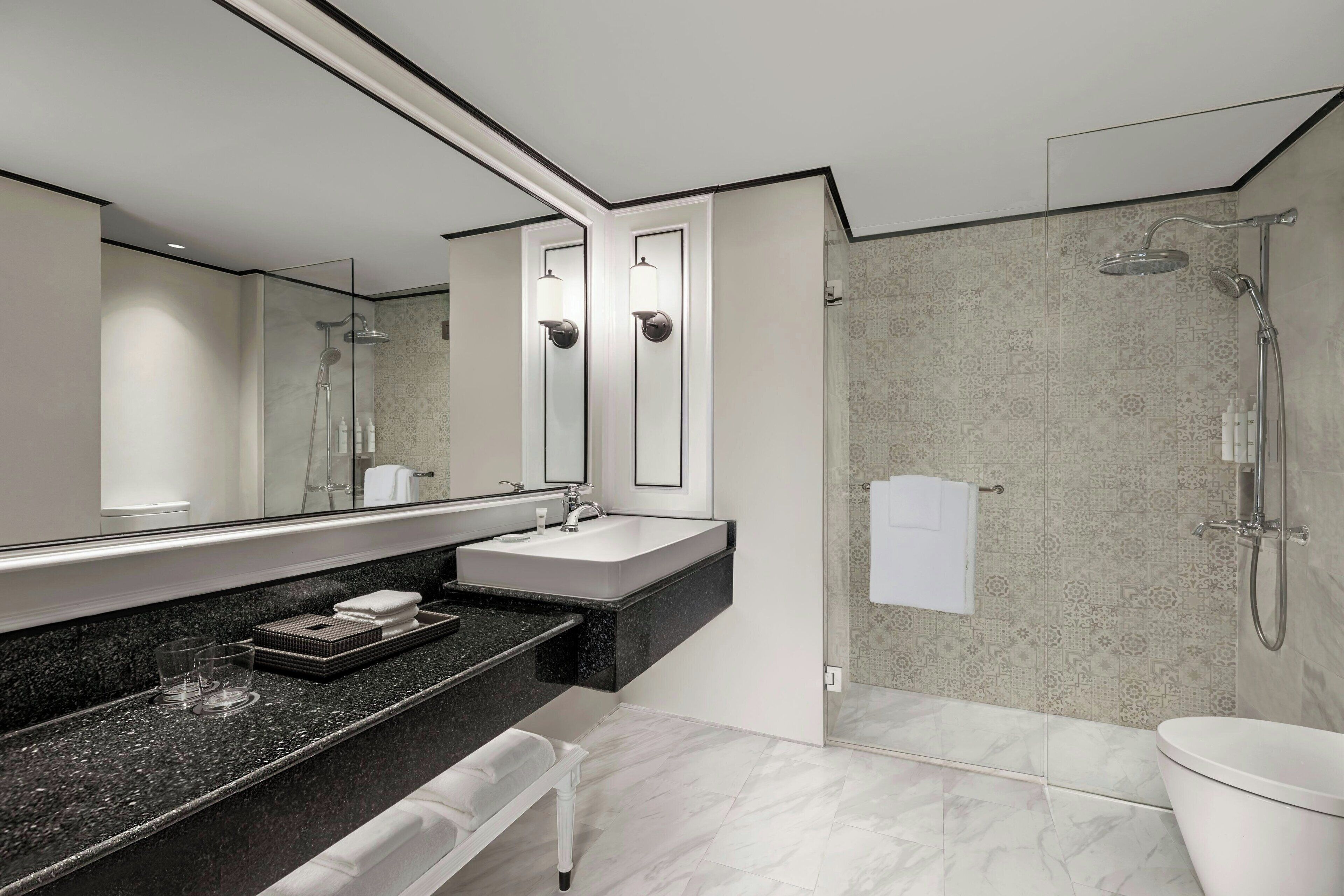 Un baño moderno con ducha de vidrio, un espejo grande, encimera negra y lavabo blanco.
