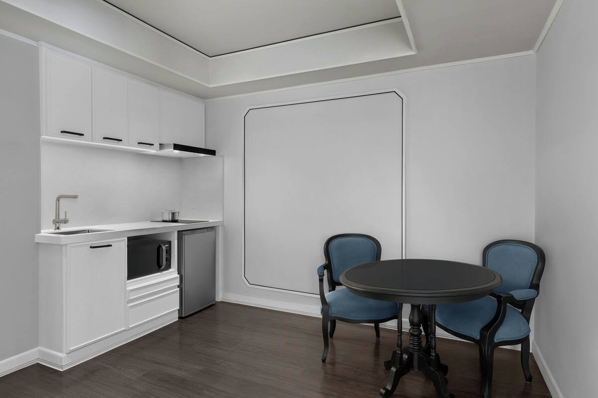Une cuisine moderne avec des meubles blancs, un four à micro-ondes et un évier. On y trouve également un coin repas avec deux chaises bleues et une table ronde.