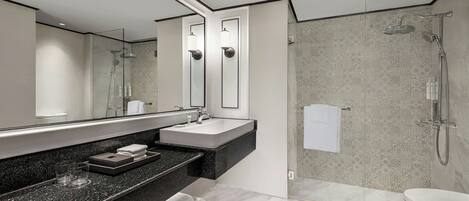 Un baño moderno con un espejo grande, un lavabo, una ducha y un inodoro.