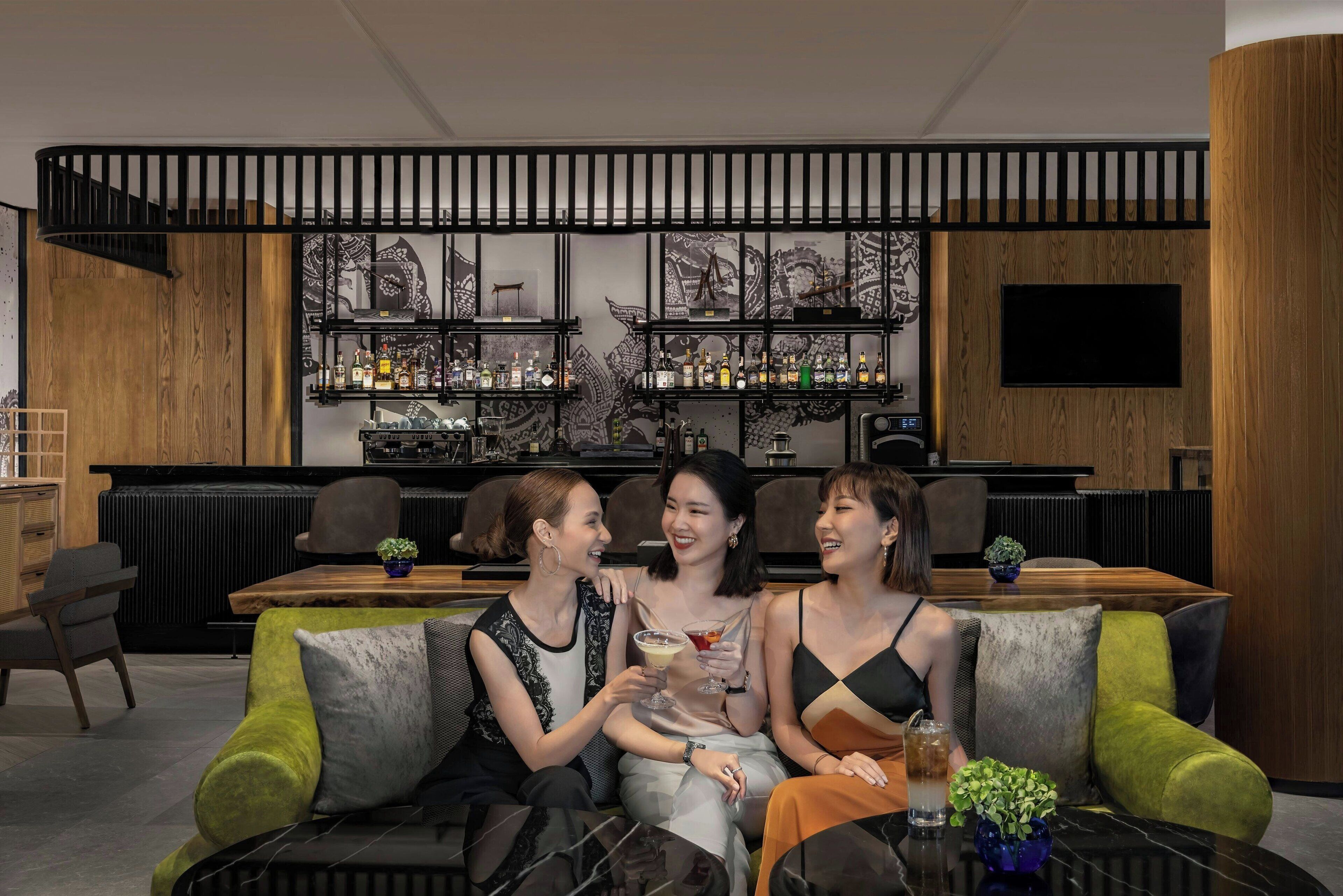 A modern bar area with a wooden bar counter, shelves with bottles, and a TV mounted on the wall.
