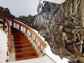 Un escalier en bois, doté d’une rampe et de marches, mène à un mur orné d’une sculpture en relief aux détails soignés.