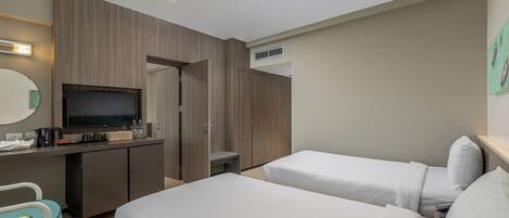 A hotel room with two beds, a desk with a television, a coffee maker, and a small table with a vase.