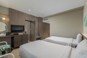 A hotel room with two beds, a desk with a television, a coffee maker, and a small table with a vase. - Pearl Hotel Phuket (Phuket)