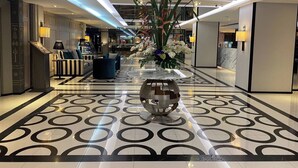 A modern hotel lobby with a geometric patterned floor, a central decorative sculpture, and a reception desk with a large vase of flowers. - Pearl Hotel Phuket (Phuket)