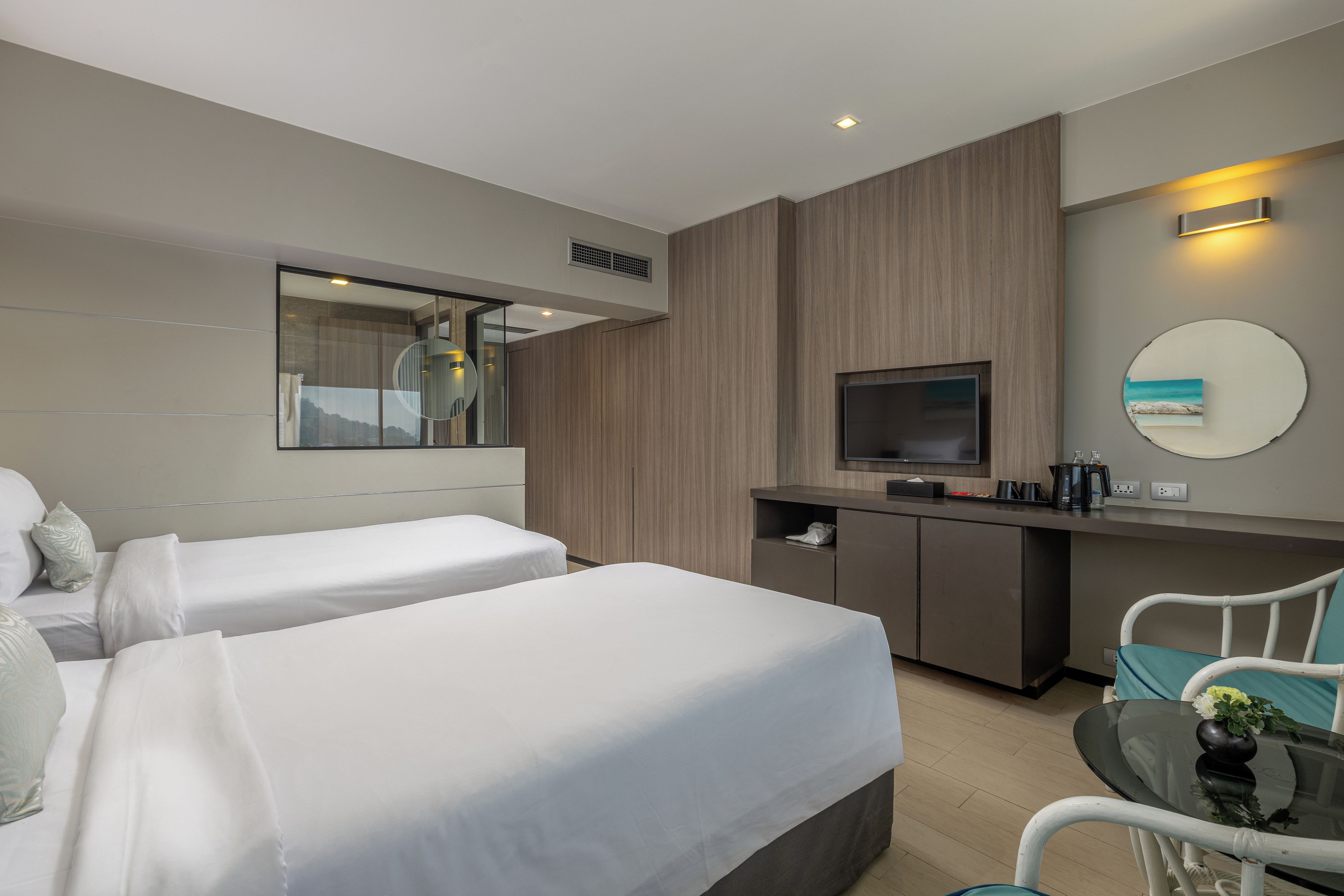 A hotel room with two beds, a desk, a television, and a mirror.