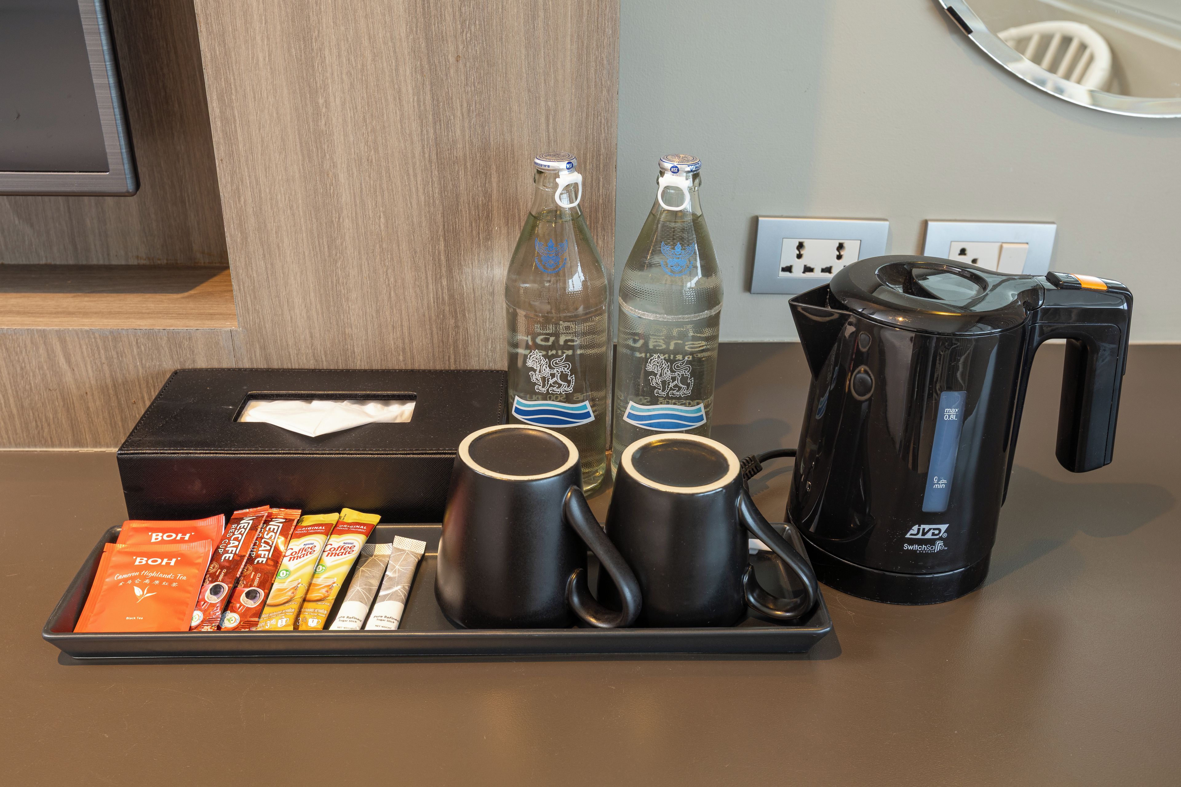 En kaffestation med kaffemaskine, to krus, en æske med kaffekapsler og to vandflasker.