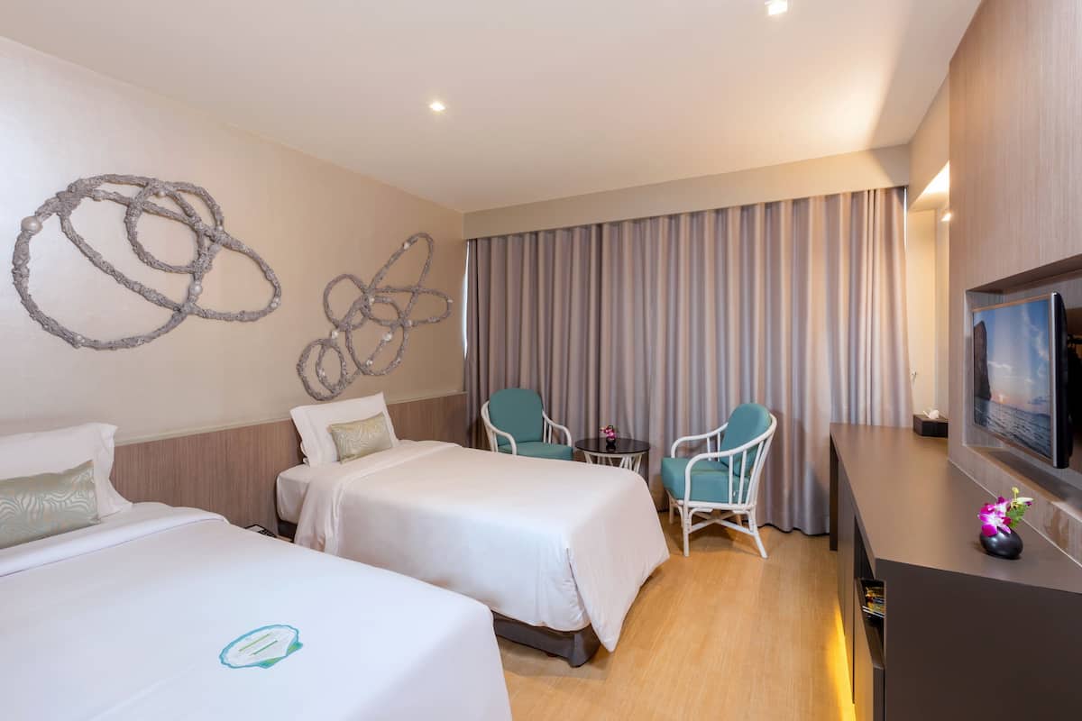 A hotel room with two beds, a desk, a chair, a TV, and a curtain.