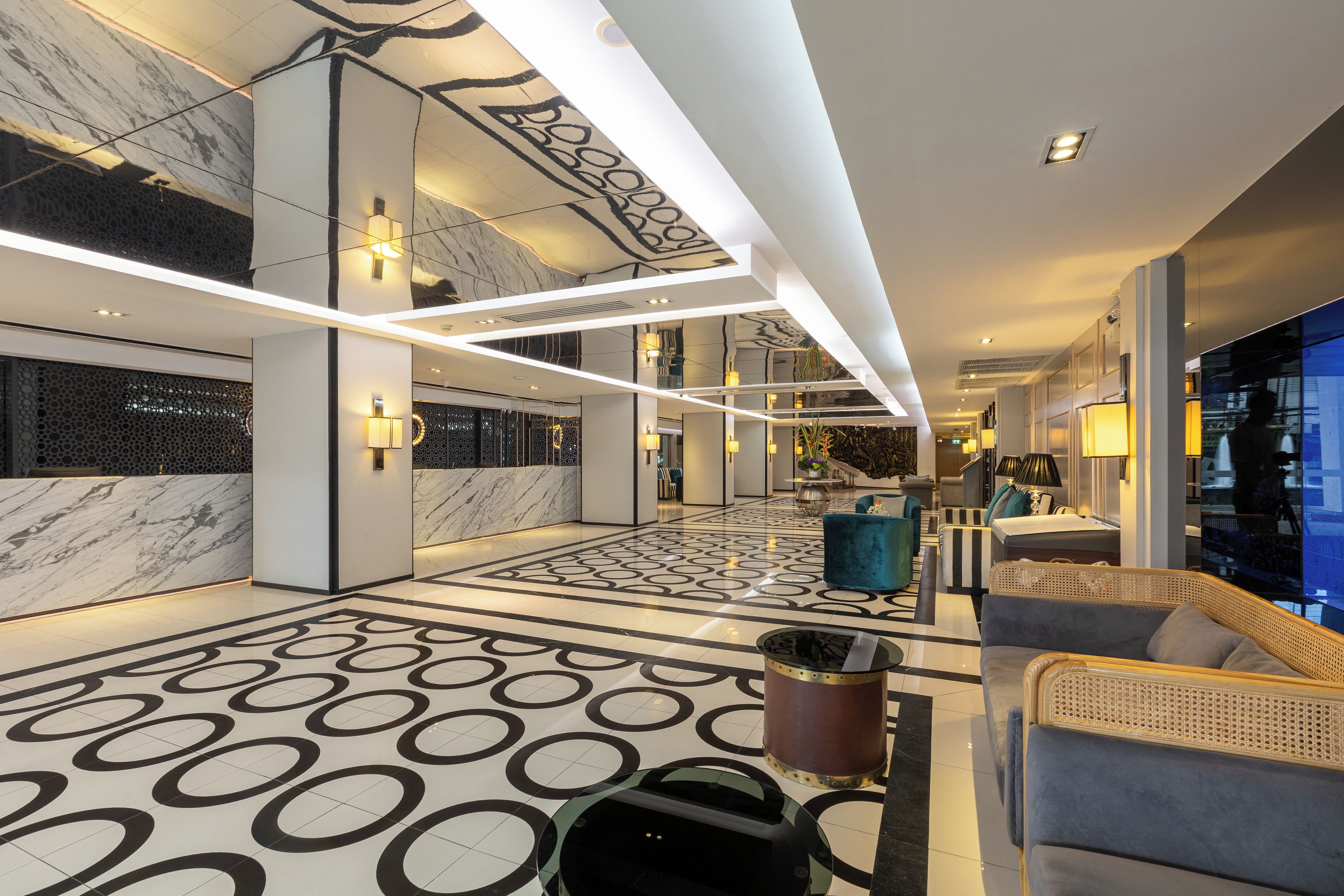 A modern lobby with a marble floor, a reception desk, and a seating area with a blue chair and a brown lamp.