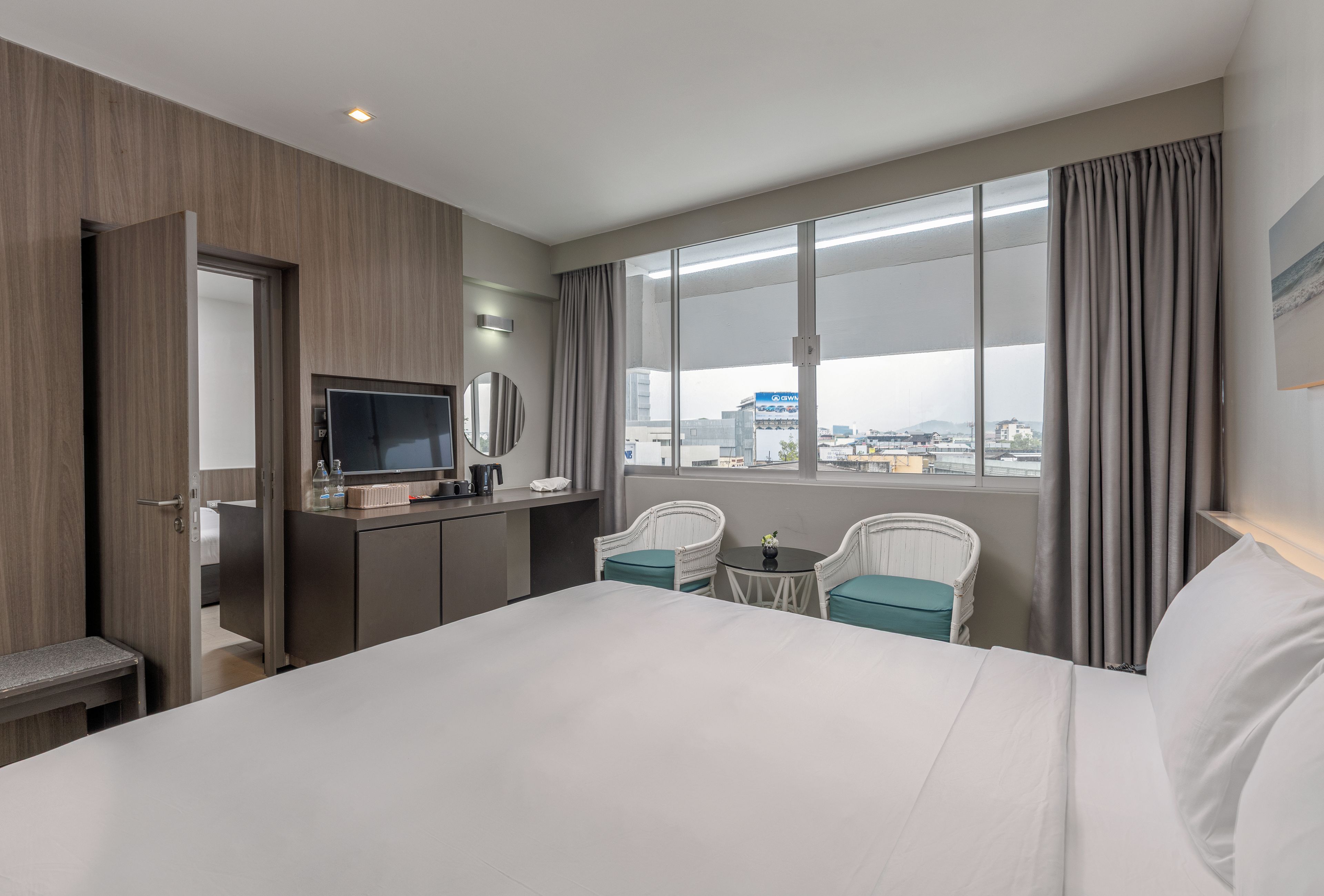 Habitación de hotel con cama, escritorio con televisor de pantalla plana, pequeña mesa con sillas y ventana con vista a la ciudad.