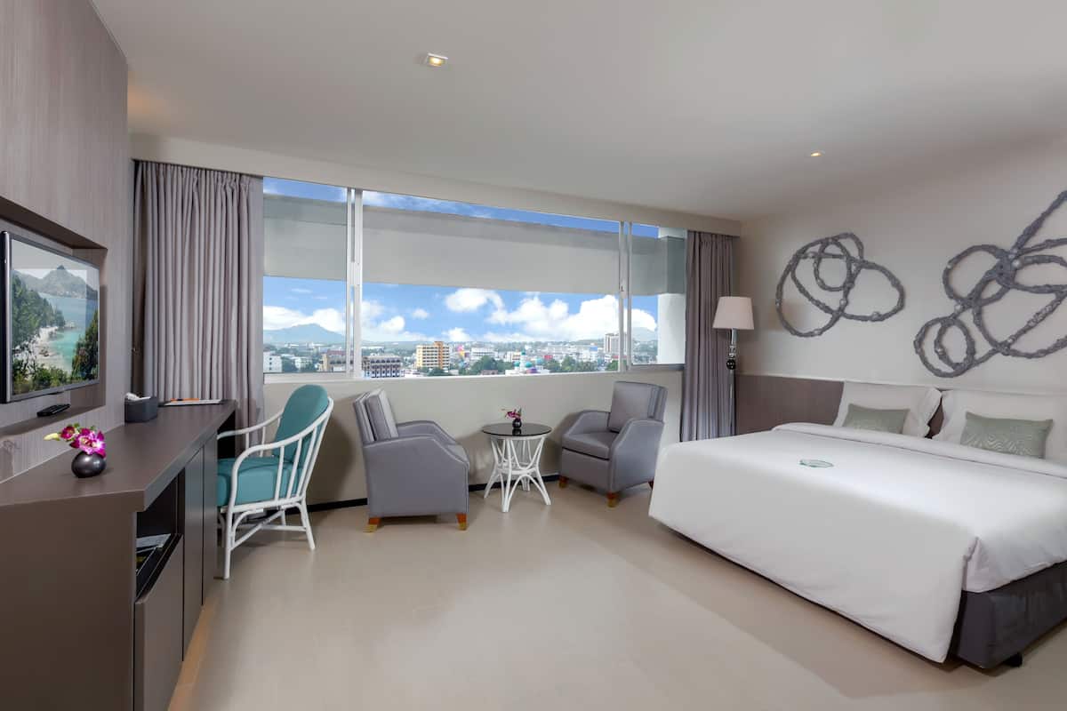 A modern hotel room with a large bed, two armchairs, a small table, and a TV.