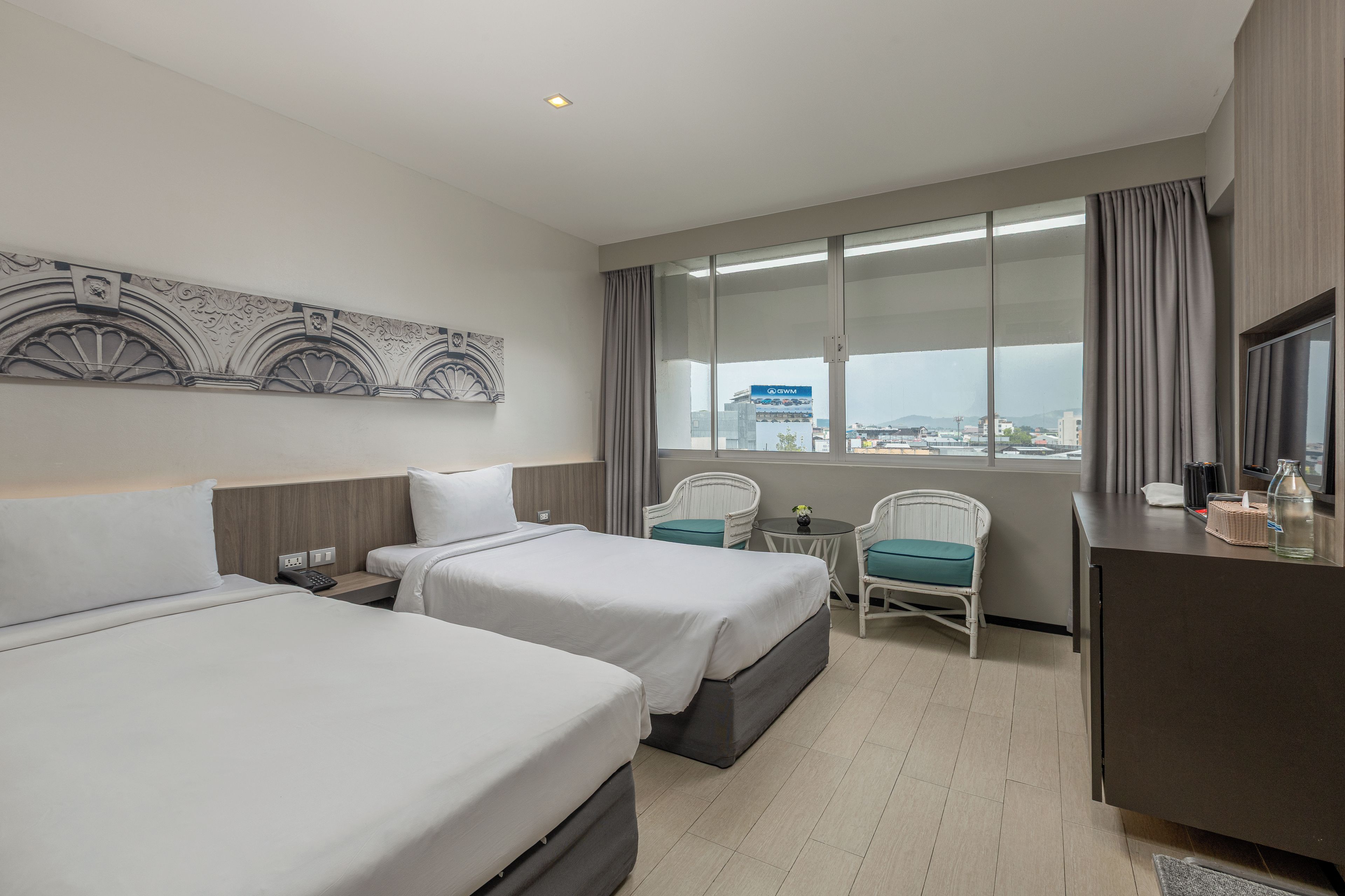 Habitación de hotel con dos camas, un escritorio, una silla y un ventanal con vistas a la ciudad.
