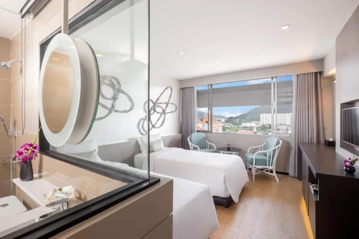 A modern hotel room with a large bed, a desk, a chair, and a view of the city.