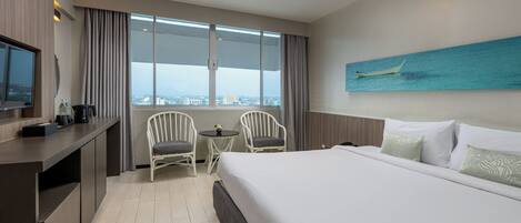 Habitación de hotel con cama, dos sillas, una mesita, televisor y un cuadro de un barco en la pared.