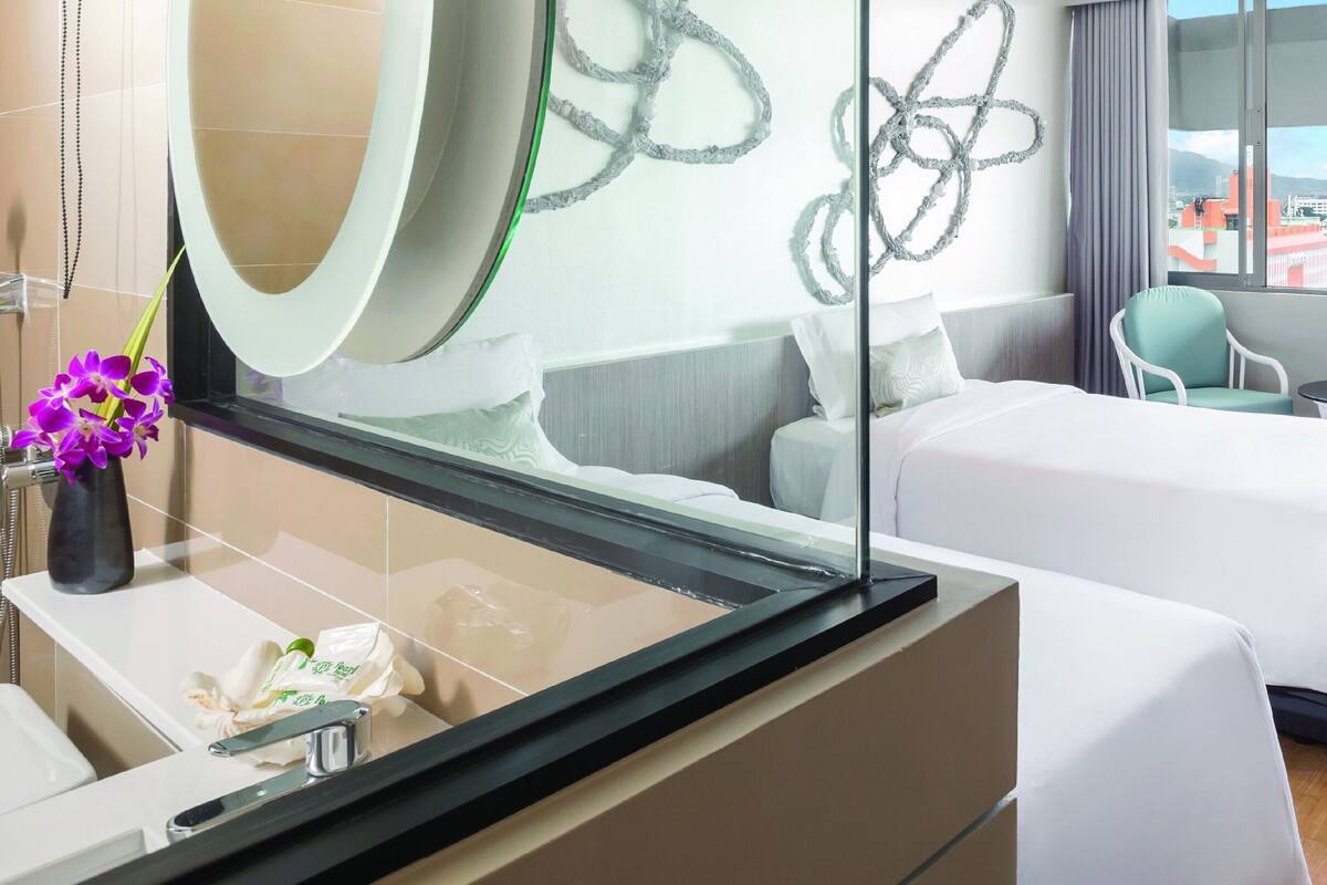 A hotel room with a bed, two chairs, a small table, a mirror, and a window with a city view.