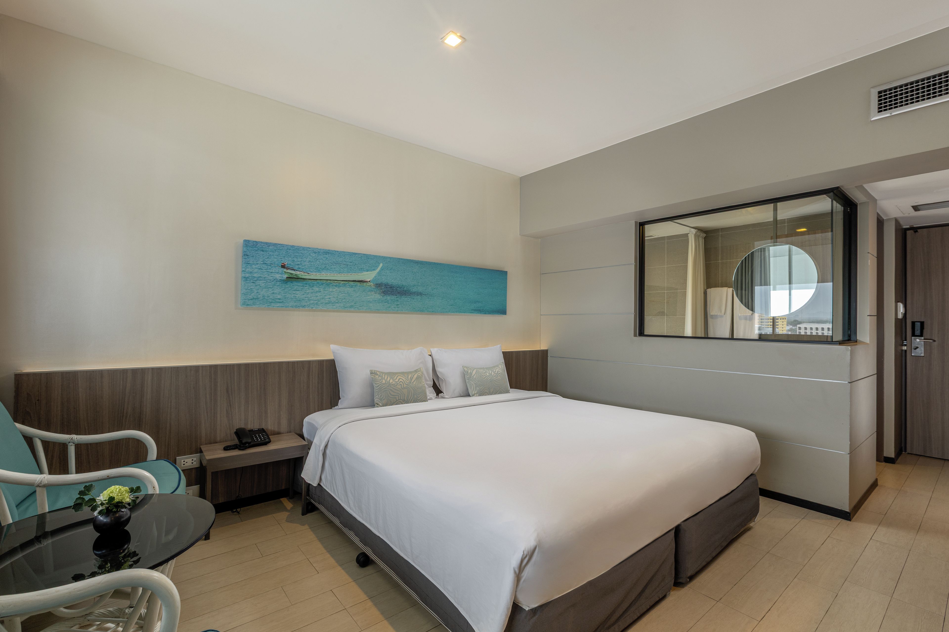 Habitación de hotel con cama, mesita de noche, silla y un cuadro de un barco en la pared.