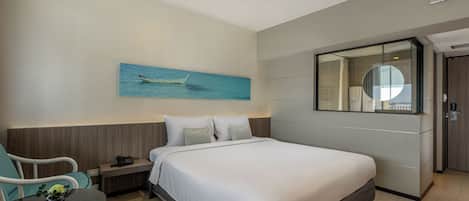 A hotel room with a bed, bedside table, chair, and a painting of a boat on the wall.
