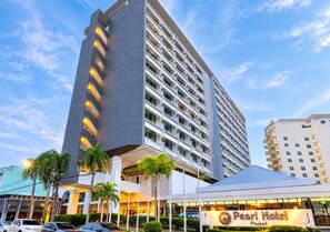 Hotel de vários andares com uma estrutura vertical imponente, placa indicando o Pearl Hotel em Phuket, e área de estacionamento com carros.