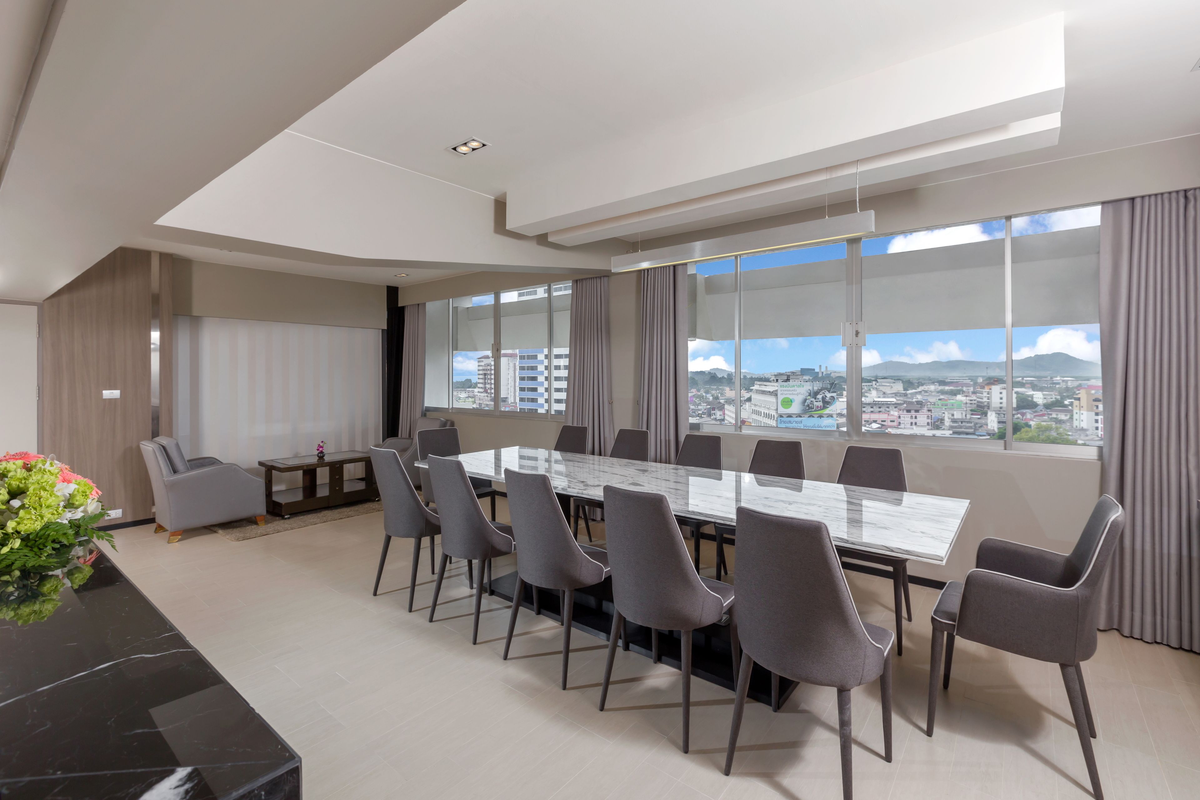 A modern conference room with a large table and chairs, large windows with city views, and a vase of flowers on a black table.