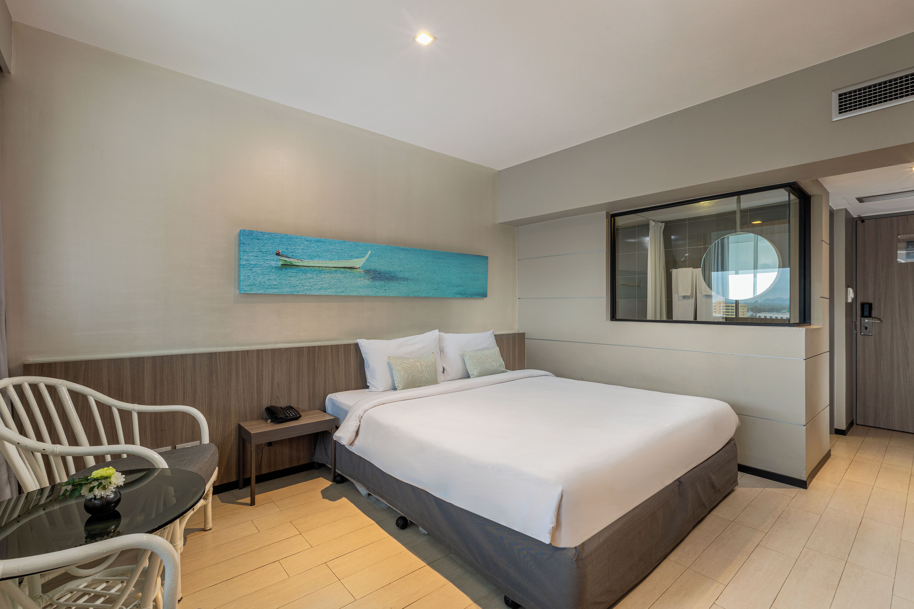 A hotel room with a bed, bedside table, chair, and a painting on the wall.