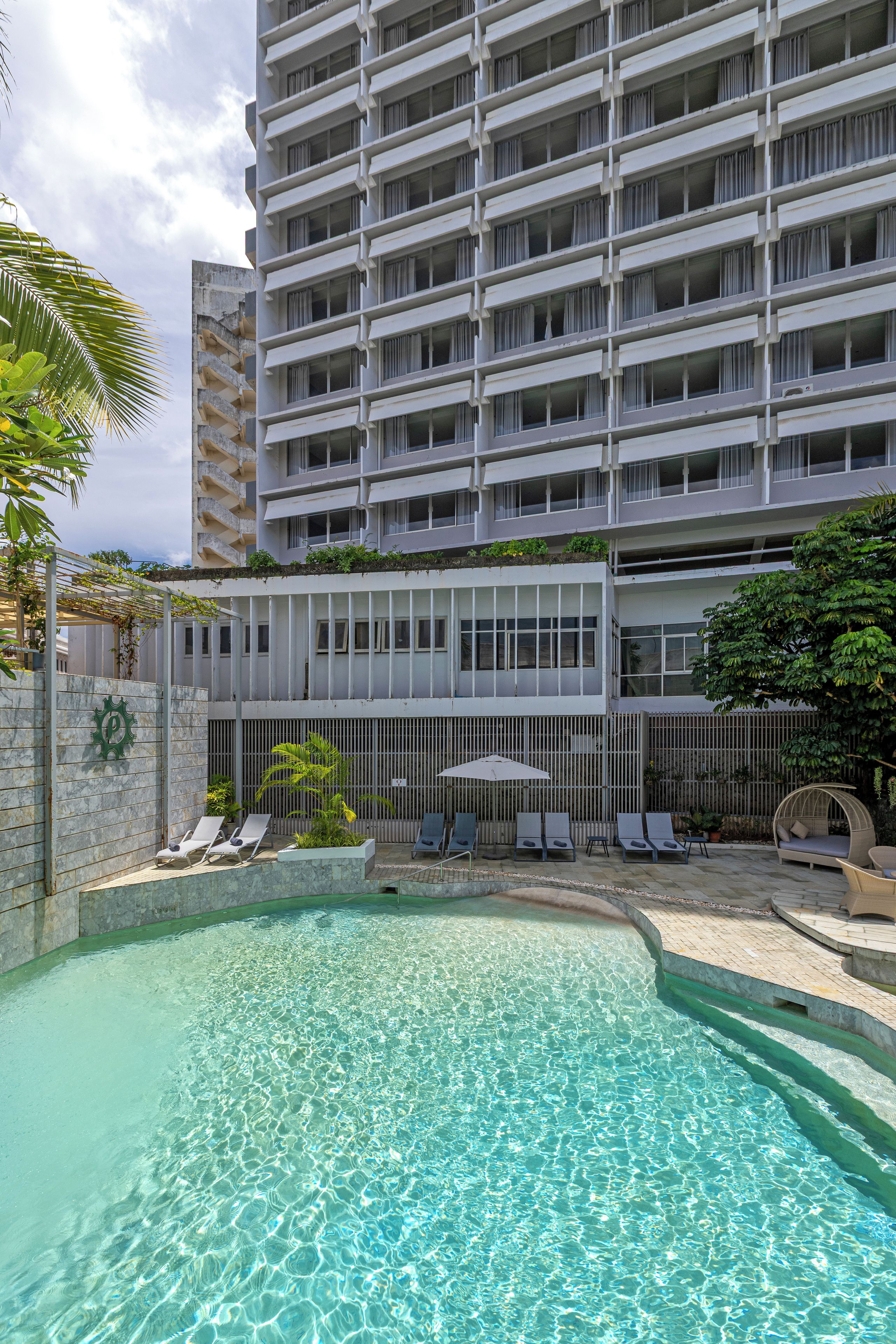 A hotel with a swimming pool, lounge chairs, and a building with multiple balconies.