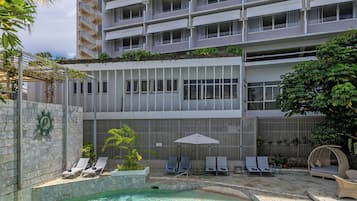 A hotel with a swimming pool, lounge chairs, and a building with multiple balconies.