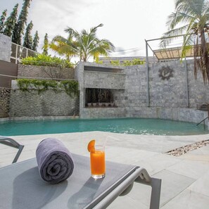 A poolside area with a lounge chair, a towel, and a glass of orange juice. - Pearl Hotel Phuket (Phuket)