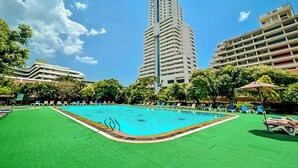 Una piscina con un césped verde, rodeada de árboles y edificios.