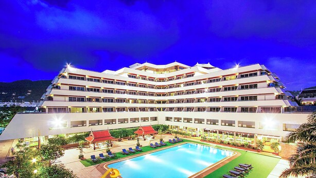 Un hotel de varios pisos con piscina, sillas de descanso y un área exterior bien iluminada.