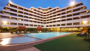 Un hotel de varios pisos con piscina, mobiliario exterior y una zona cubierta.