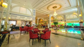 A spacious lobby with a central fountain, red patterned chairs, and a reception area with a counter and chairs.