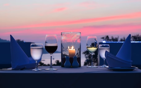 A table set with four glasses of wine, a lit candle, and two salt and pepper shakers, set against a sunset backdrop.