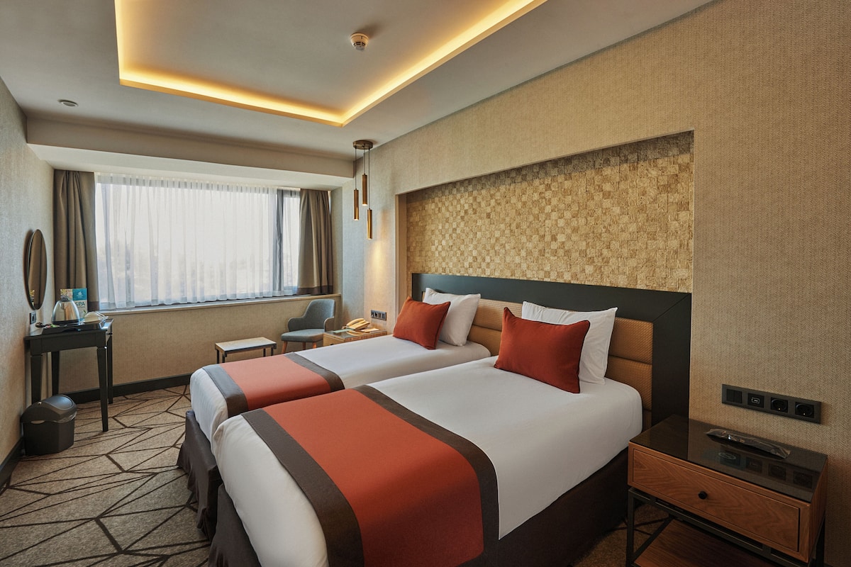 Une chambre d’hôtel avec deux lits, un bureau, une chaise et une fenêtre avec des rideaux.
