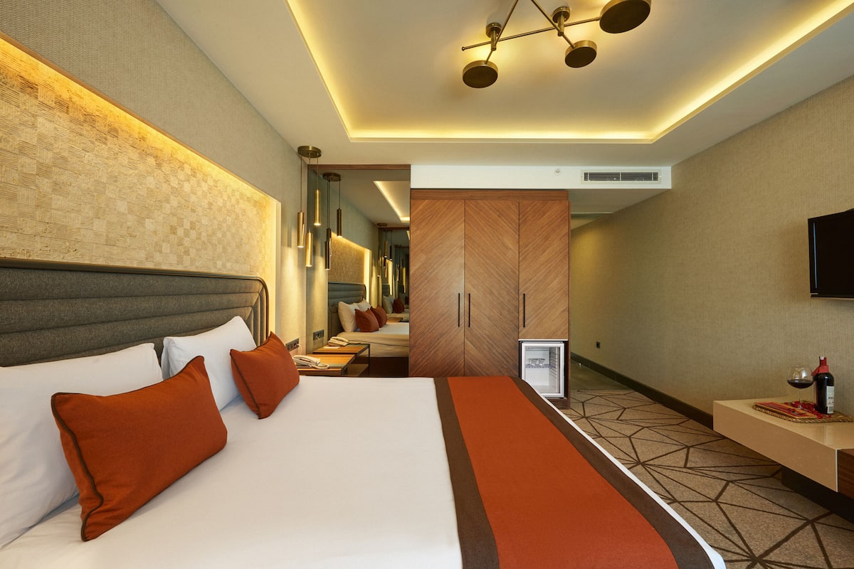 Une chambre d’hôtel moderne avec un grand lit, une armoire en bois, une télévision et un minibar.