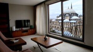 A modern living room with a large window, a flat-screen TV, a wooden coffee table, and a sofa. - Grand Hotel Gulsoy (Istanbul)