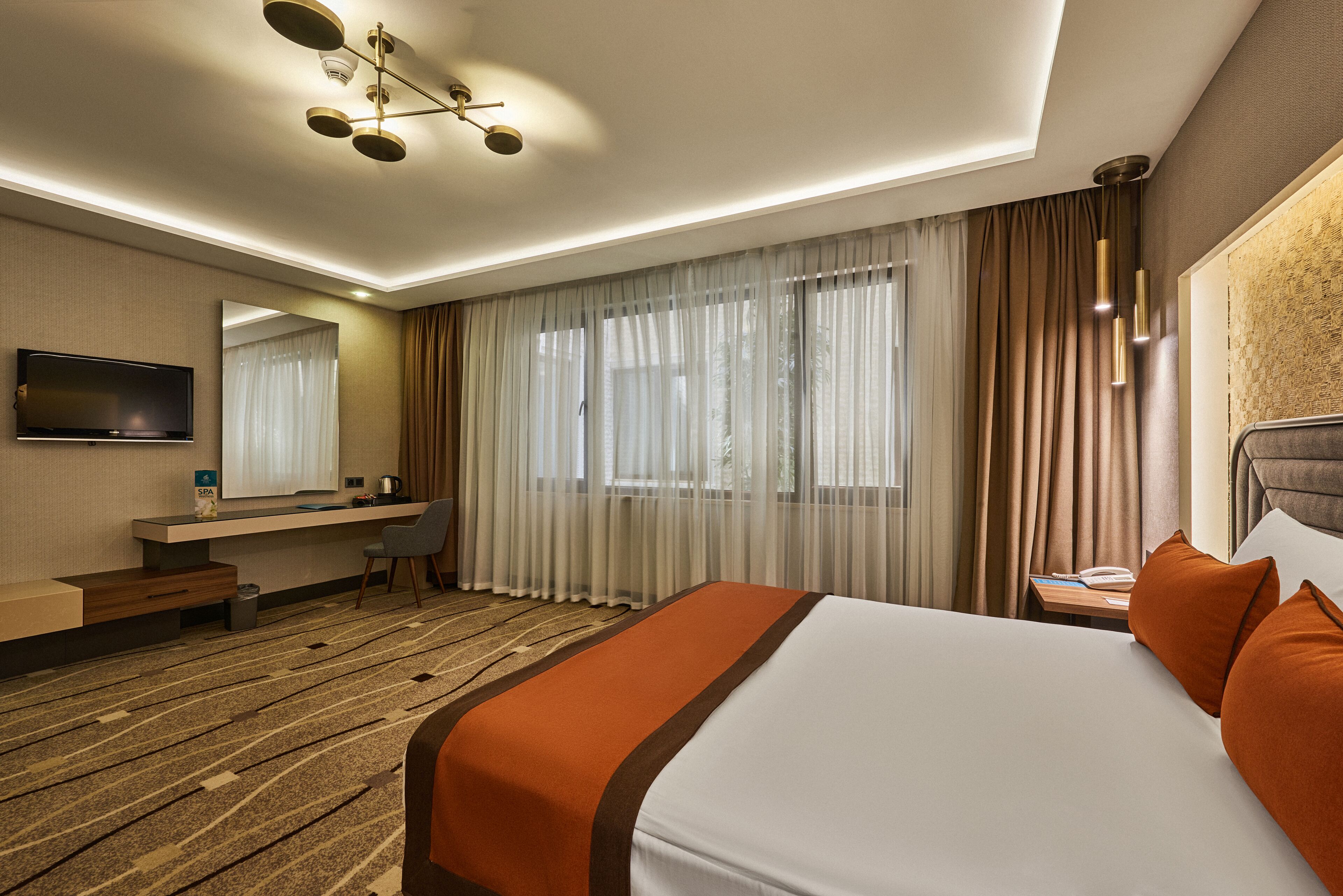 A hotel room with a large bed, a desk with a chair, a television, and a window with curtains.