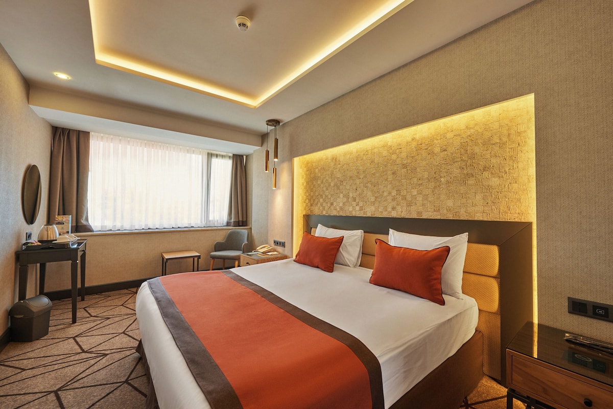 Une chambre d’hôtel avec un grand lit, un bureau, une chaise et une fenêtre avec des rideaux.
