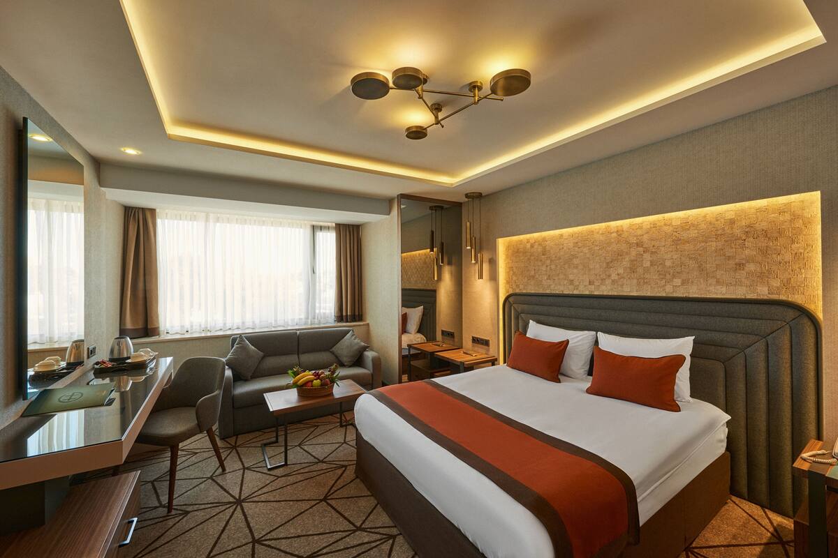 Une chambre d’hôtel comprenant un lit, un bureau, une chaise, un canapé, une table de chevet et un grand miroir.