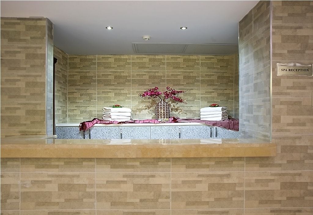Un espace d’accueil pour le spa, avec un mur recouvert de carreaux, un comptoir d’accueil et un panneau indiquant la réception du spa.