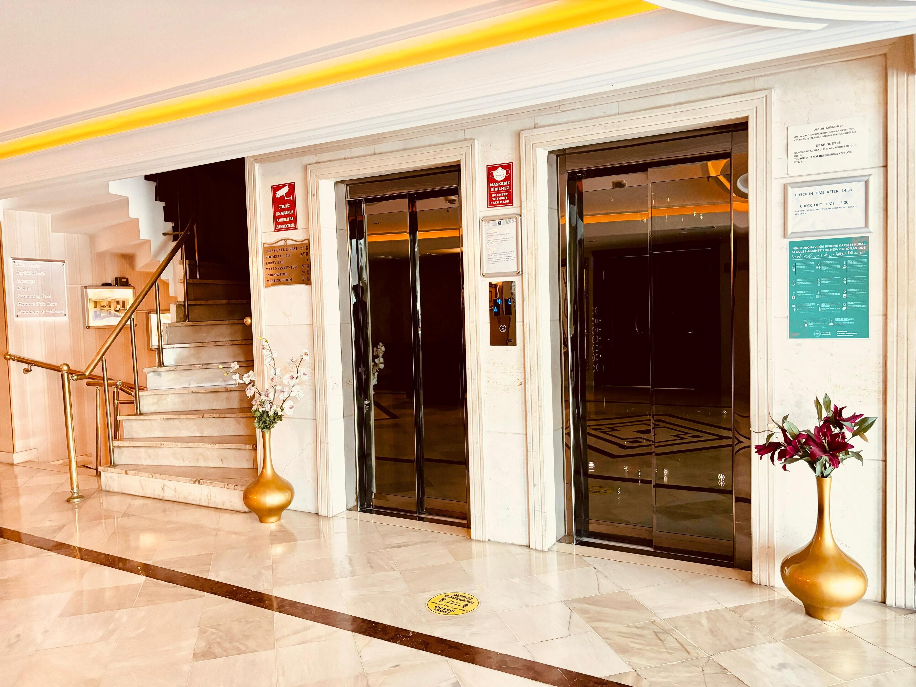 A hotel lobby with a staircase, elevators, and a reception desk.