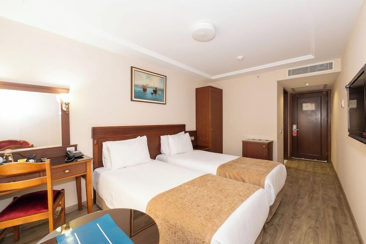 A hotel room with two beds, a desk with a telephone, a chair, a small table, and a door.